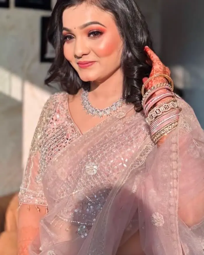 A soft-base makeup look in a pale pink organza saree, with a warm eye and a diamond necklace
