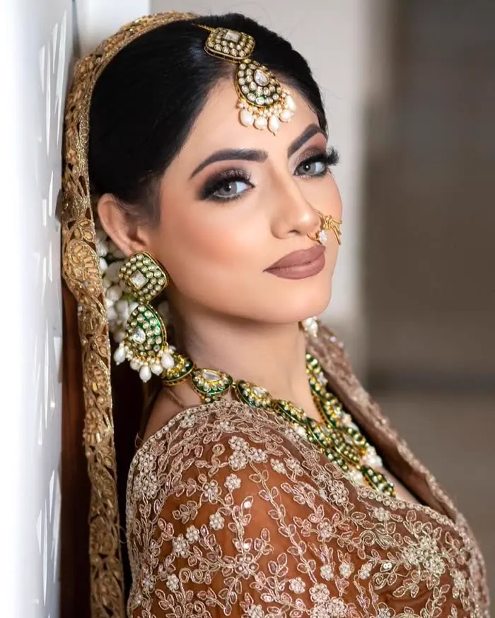 A profile with a smoky eye and a deep brown lip, a gold kundan maang tikka and a nose ring