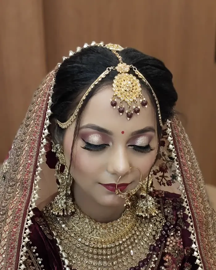 Eyes down in a full bridal look: shimmer lids, a red lip, gold maang tikka and layered kundan