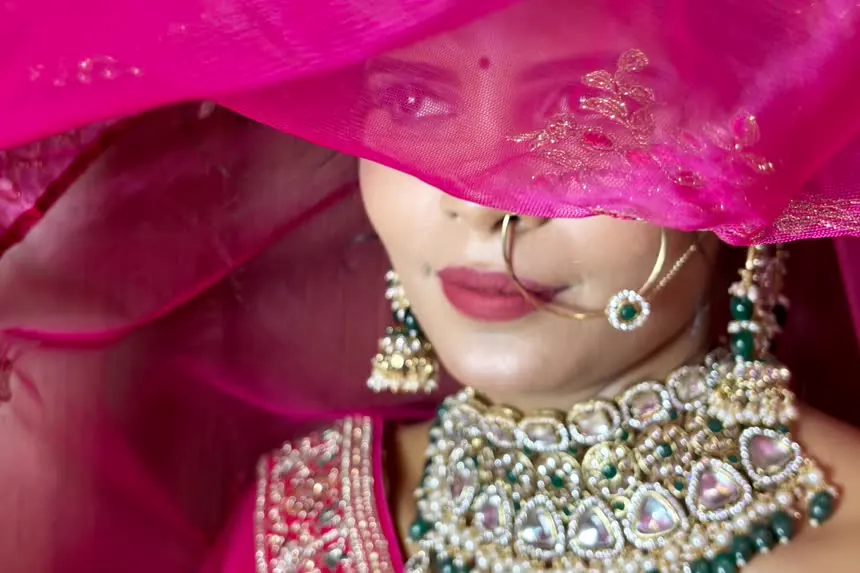 A bride under a pink dupatta, with a kundan choker and a nose ring