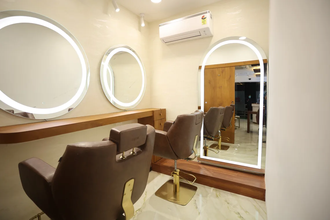 The studio floor: brown chairs before round lit mirrors, a tall arched mirror beyond, marble underfoot.