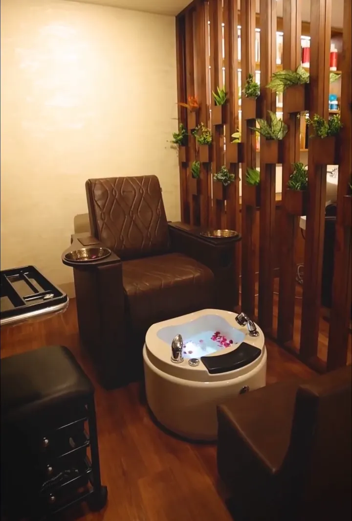 A pedicure chair with a steel footrest bowl beside a white foot spa basin on a wooden floor.
