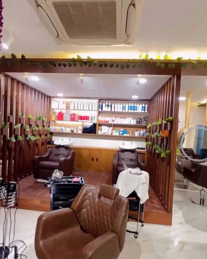 Two wash basins with reclining chairs under a shelf of hair products, and a styling chair in the foreground on an empty salon floor.