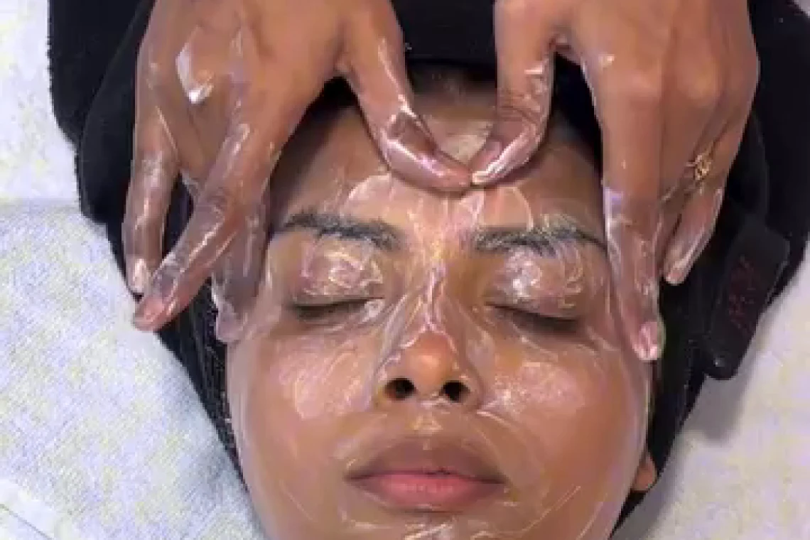 A facial in progress, both hands working across the forehead, eyes closed.