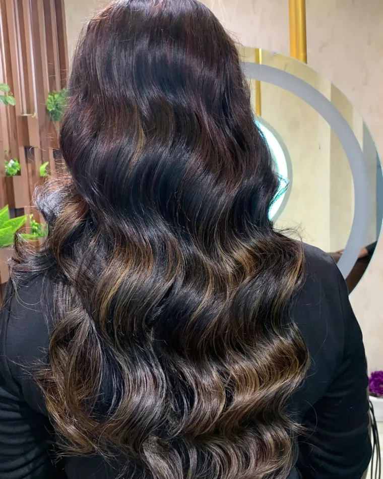 Long waved hair seen from behind at the round lit mirror in the studio.