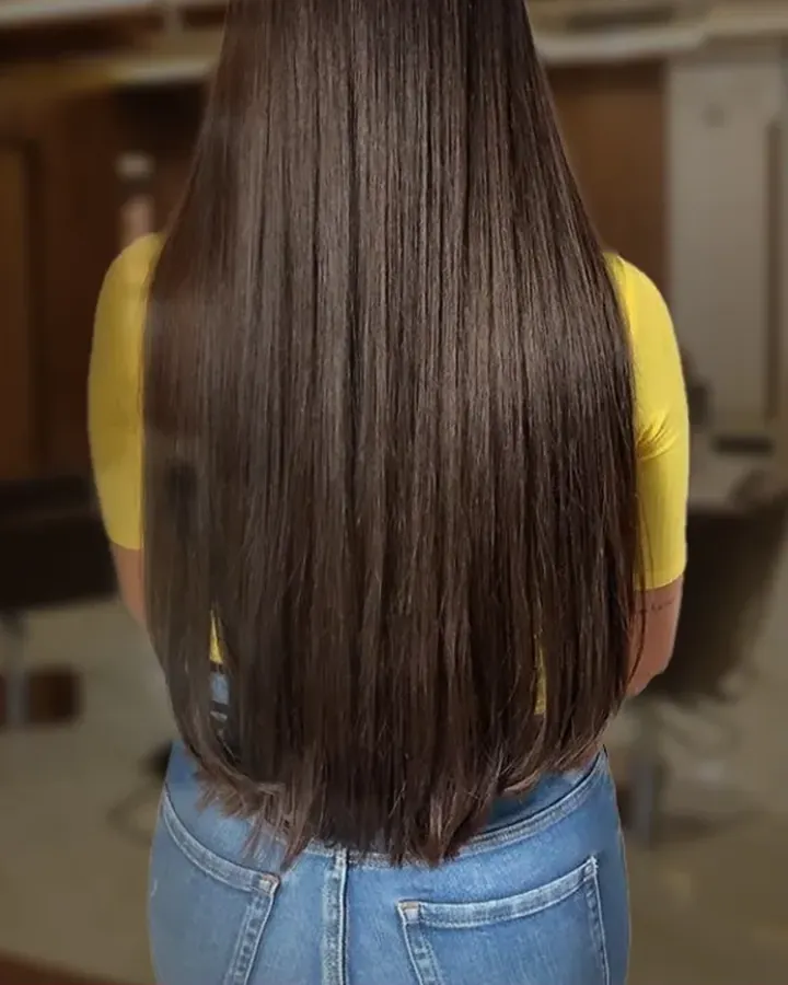 A woman in a yellow top with her back to the camera, long straight dark hair to the waist.