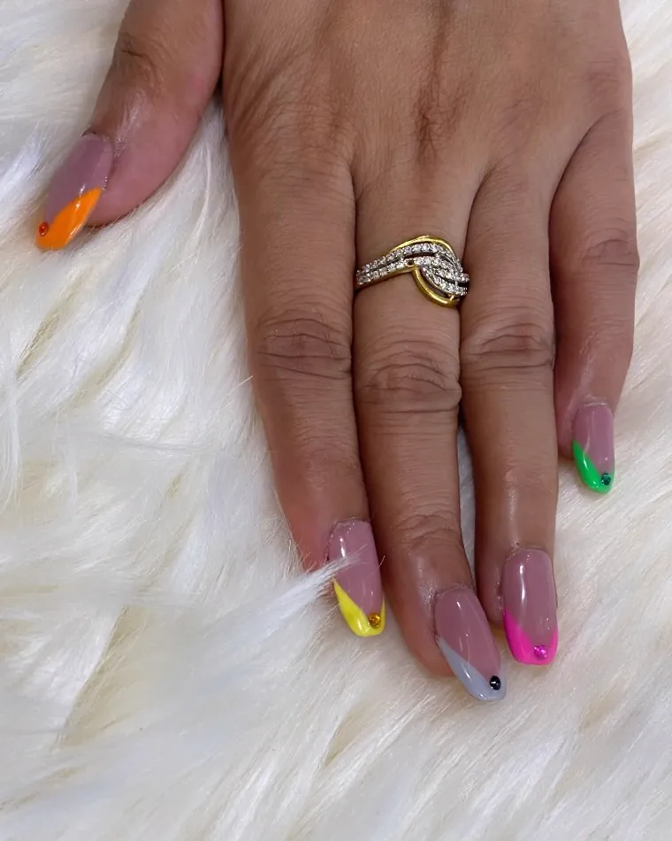 A hand resting on a soft white rug, clear pink nails with each tip painted a different colour.