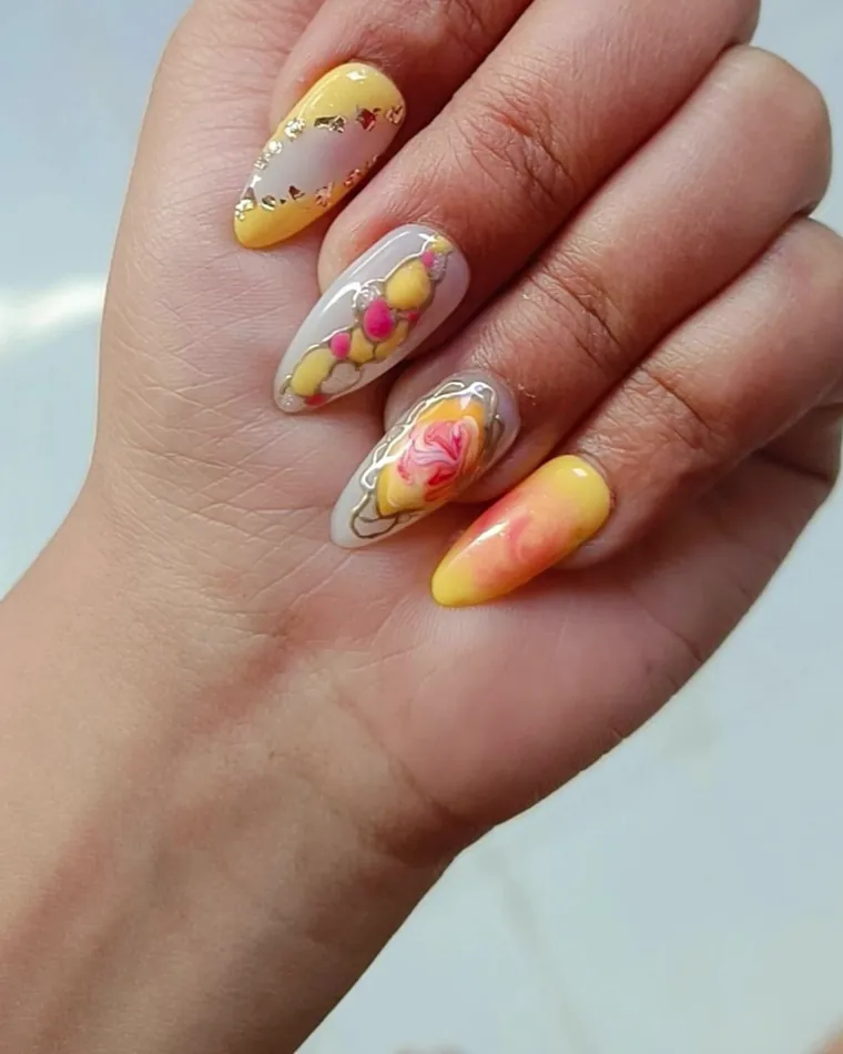 Long almond nails in yellow and cream with hand-painted flowers and gold leaf detail.