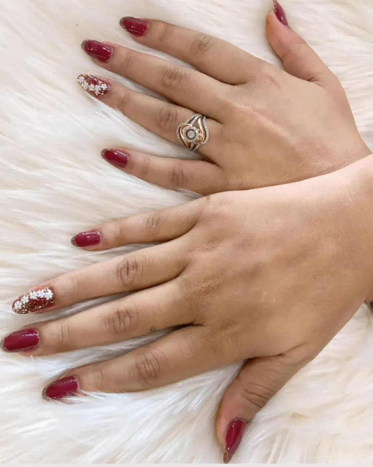Two hands on a soft white rug with deep red nails and two accent nails in gold and white flowers.