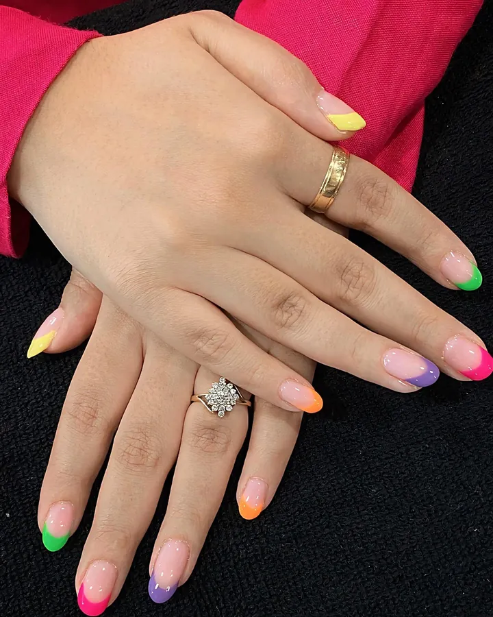 Two hands on a black towel with almond nails in neon green, pink, purple, orange and yellow French tips.