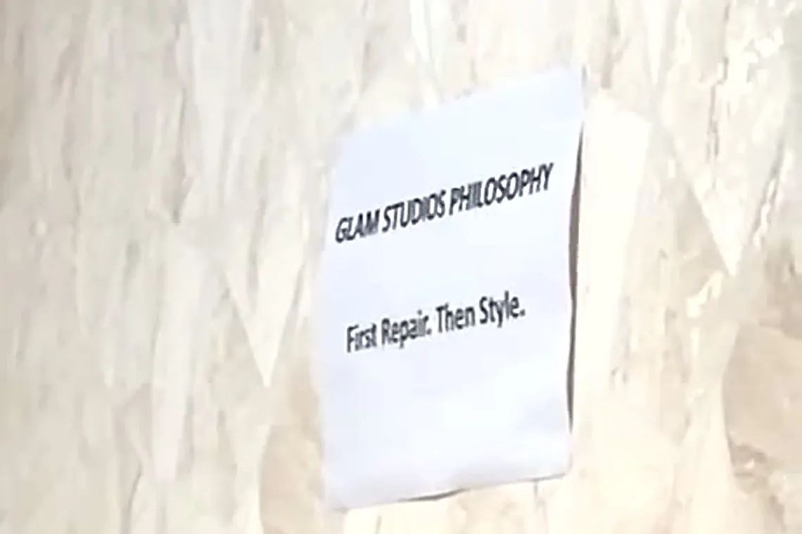 A printed sign on the studio wall reading Glam Studios Philosophy, First Repair. Then Style.