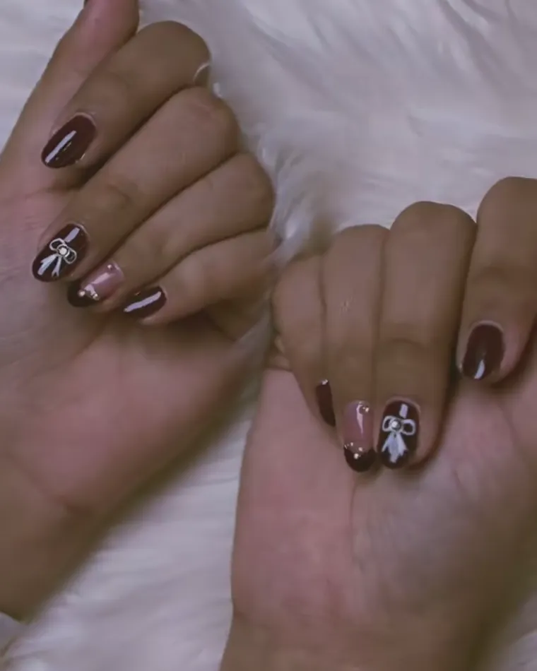 Two hands on a soft white rug, nails painted deep brown, two of them carrying a small white bow.