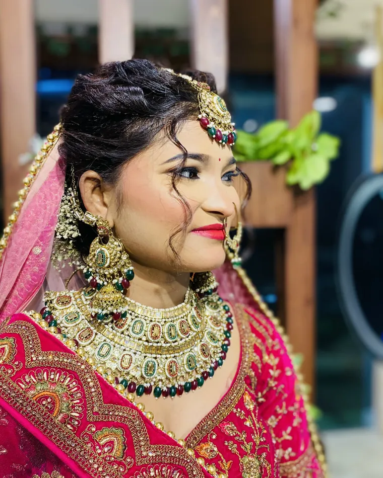 Close profile of an occasion look — textured updo, gold maang tikka and a kundan collar.