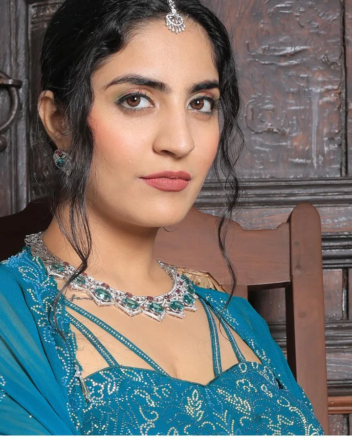 A teal embroidered outfit and a green stone necklace, seated against a carved door, from our styled shoot.