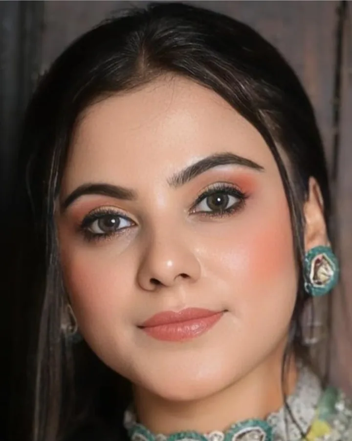 A close beauty portrait: warm coral eyes and cheeks, a soft peach lip, a green stone earring.