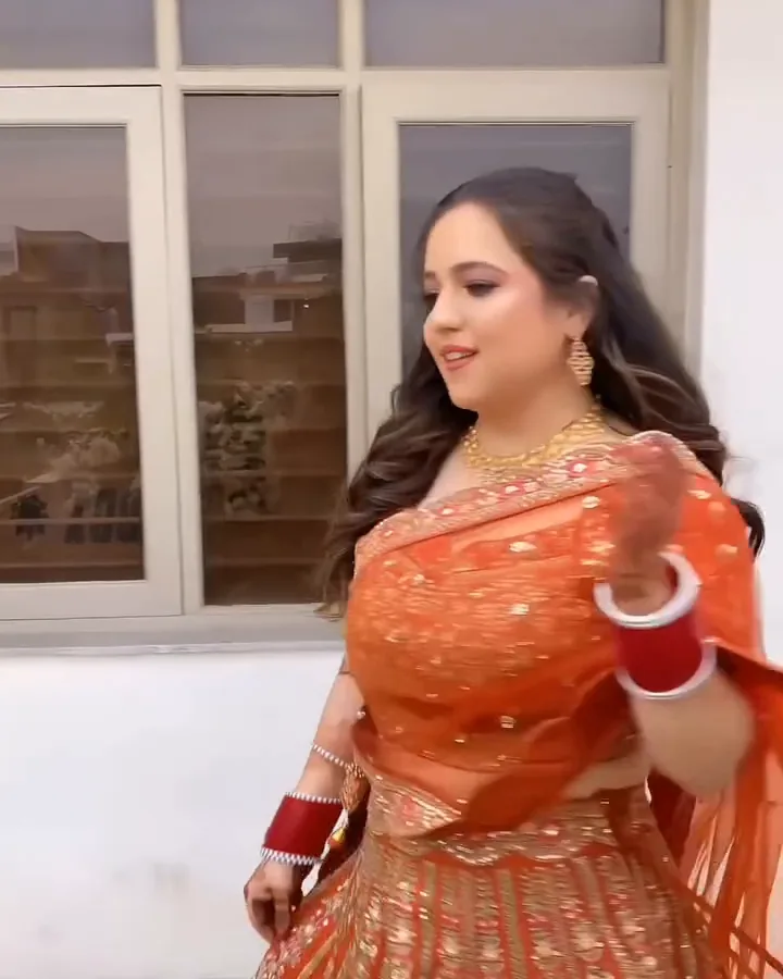 An orange embroidered lehenga with red and white bangles, turning on a terrace, from our styled shoot.