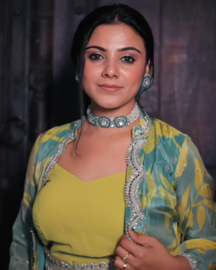 Mehendi look: a lime-yellow gown with a printed cape, standing at a dark carved door.