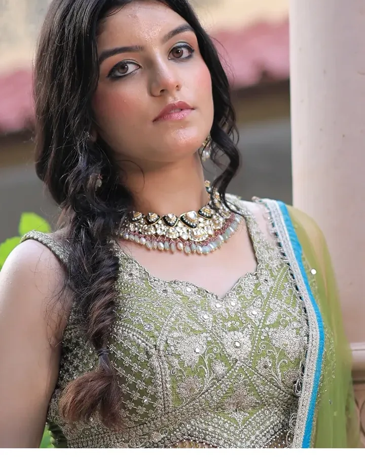 Mehendi look: a green embroidered outfit, a fishtail braid and a kundan choker in a courtyard.