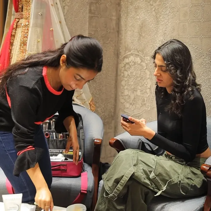 An artist leans over an open makeup kit beside a seated woman waiting in a chair at an on-location booking.