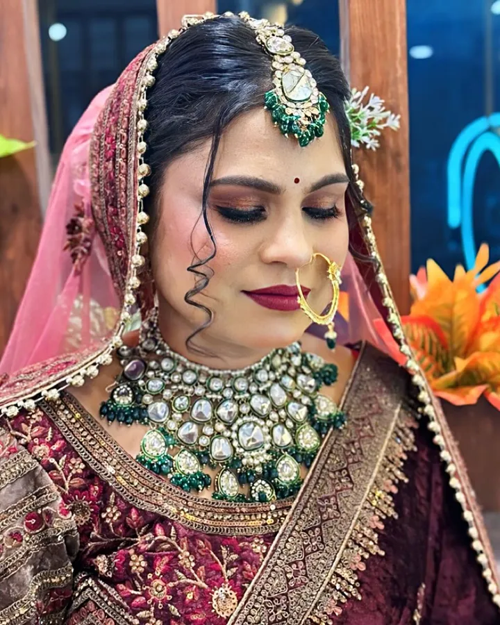 The same bride looks down in profile, her heavy green and white kundan necklace and pink veil filling the frame.