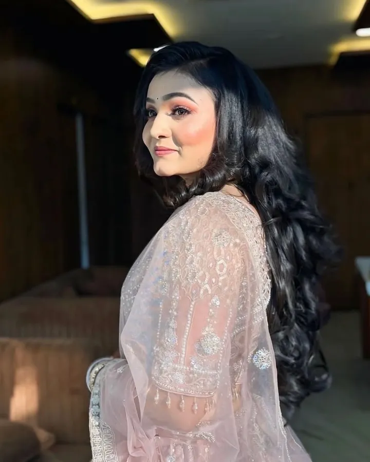 The same woman turns away from camera to show long blow-dried curls falling over the back of her blush embroidered saree.
