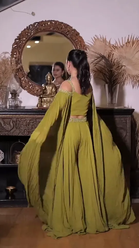 Mehendi look from the styled shoot: a lime-green outfit with fluted cape sleeves, seated in a carved chair by a dark wooden door.