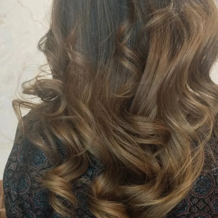 Close back view of long hair curled into loose ringlets, dark at the roots and lightening to a sandy balayage through the ends.