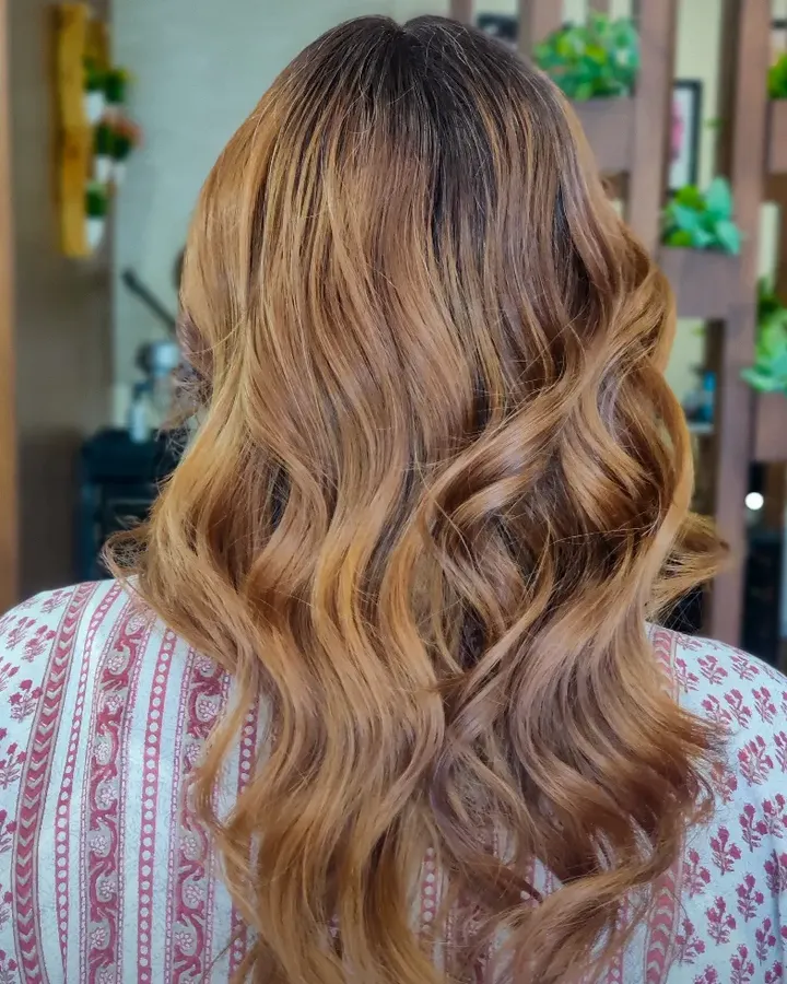 Back view of shoulder-length hair blow-dried into loose waves, a honey-gold balayage lightening away from the darker roots.