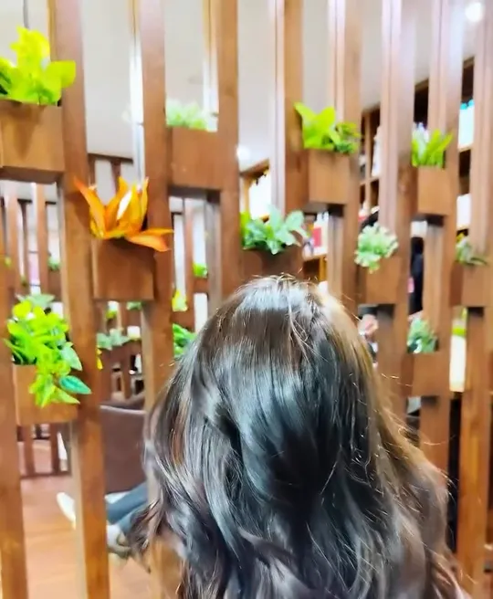 Back view of a woman in a black top lifting her own hair with her right hand, which carries green and red thread bangles.