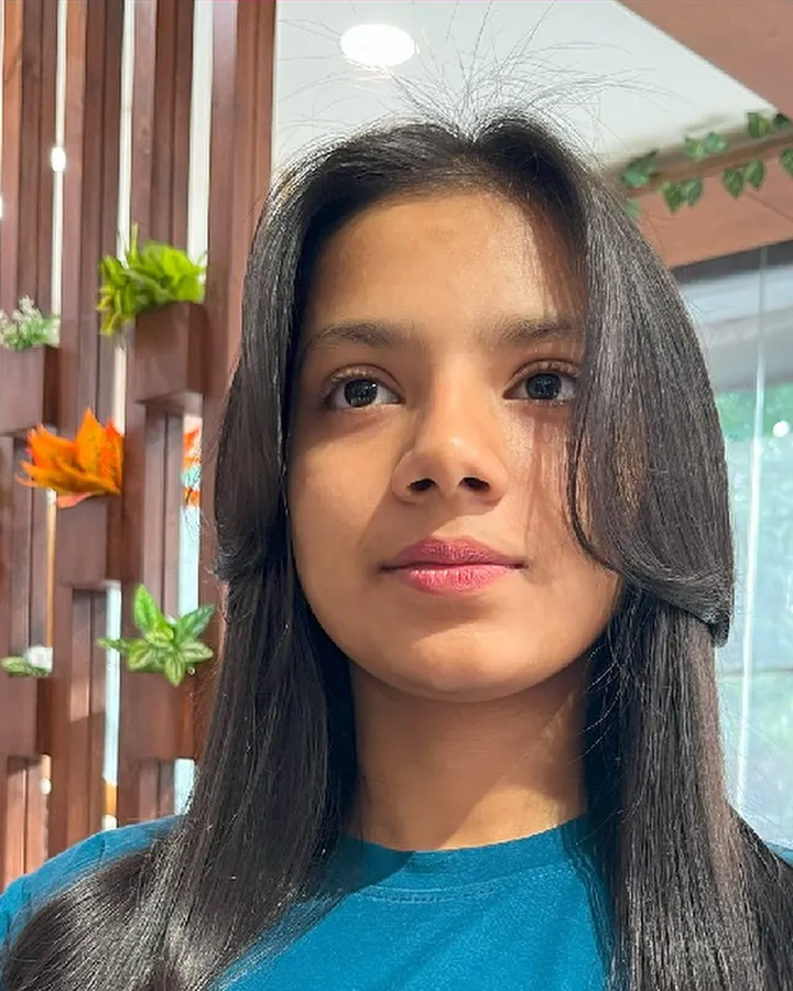 A young woman with long, straight, glossy blow-dried hair looks at the camera in the salon.