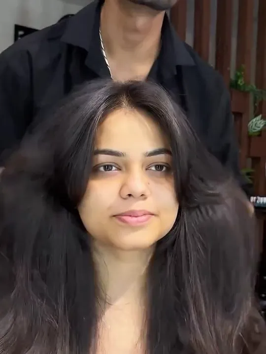 A male stylist in black finger-styles and tousles a seated woman's long dark hair, working through the lengths.