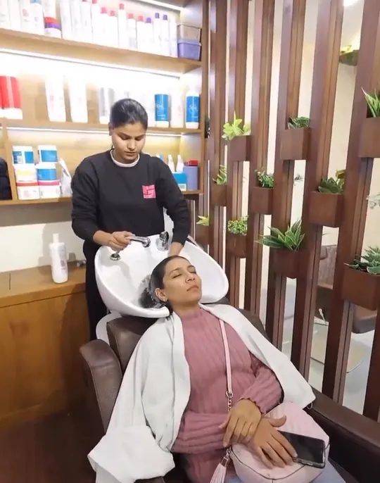 A stylist rinses and lathers a reclining client's hair at the salon's white backwash basin.