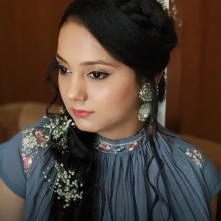 A close portrait of a woman with a braided updo dressed with small white flowers and soft occasion makeup.