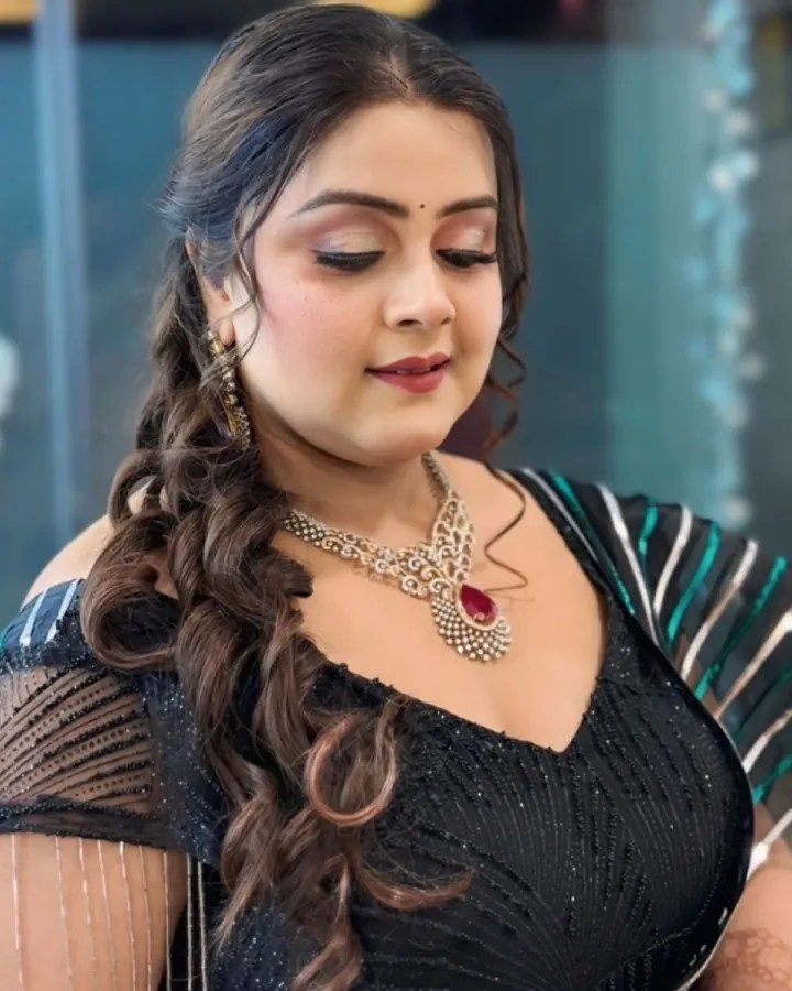 A portrait of a woman looking down and to her left, in a black sequinned blouse and saree with a green-and-white striped pallu over one shoulder.