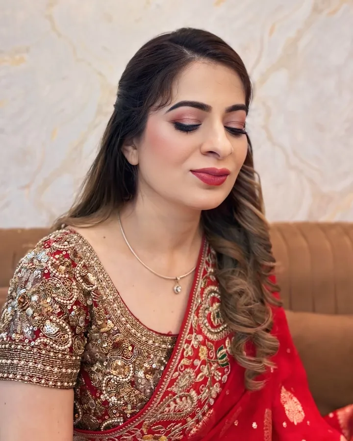 A close portrait of a woman seated with her eyes closed and chin slightly down, in a red saree over a heavily worked gold sequin-and-pearl embroidered blouse.