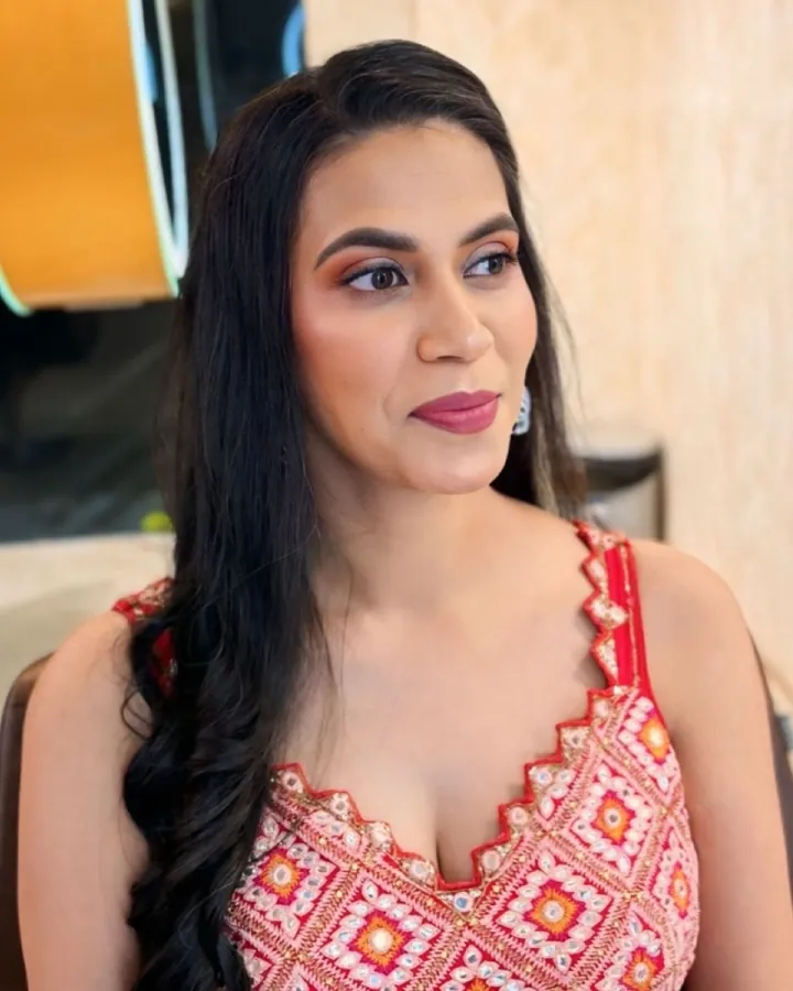 Two tight portraits of the same woman in a red-and-pink mirror-work embroidered sleeveless outfit, seated in a salon chair against a beige textured wall with a .