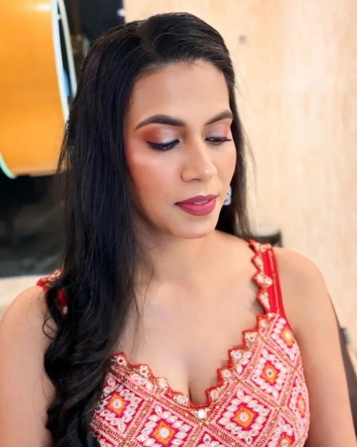 Two tight portraits of the same woman in a red-and-pink mirror-work embroidered sleeveless outfit, seated in a salon chair against a beige textured wall with a .