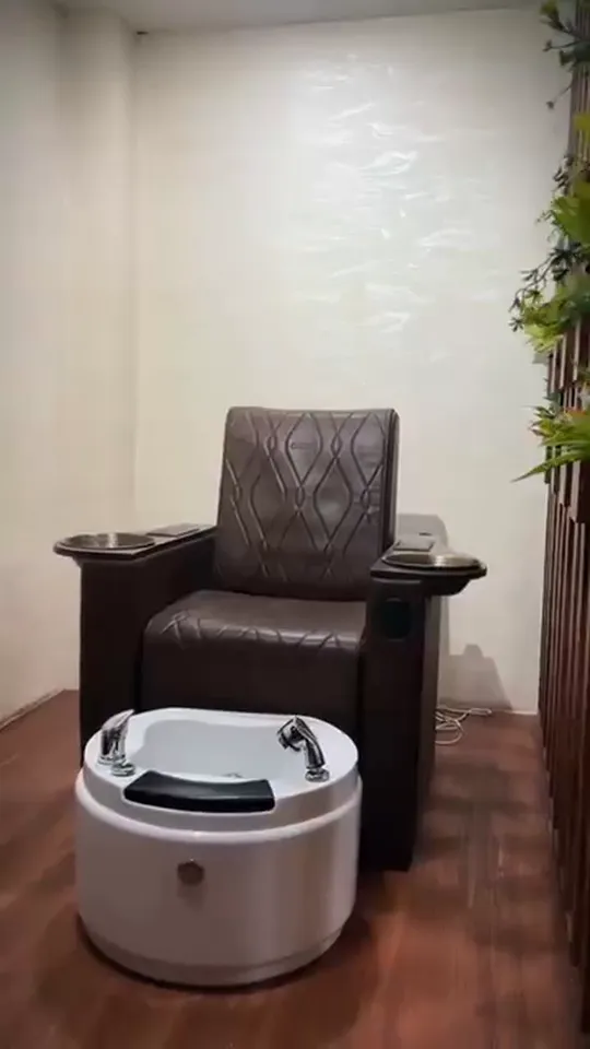 A handheld walk through the salon past wash-station recliners, lit shelves of hair product and a pedicure chair, ending with staff working on seated clients at the styling stations.