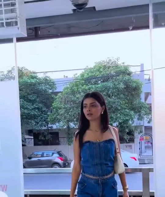 At the curved reception counter, a man in a black Glam Studios polo stands behind the desk facing a young woman client in a denim top and cargo jeans with a cre.