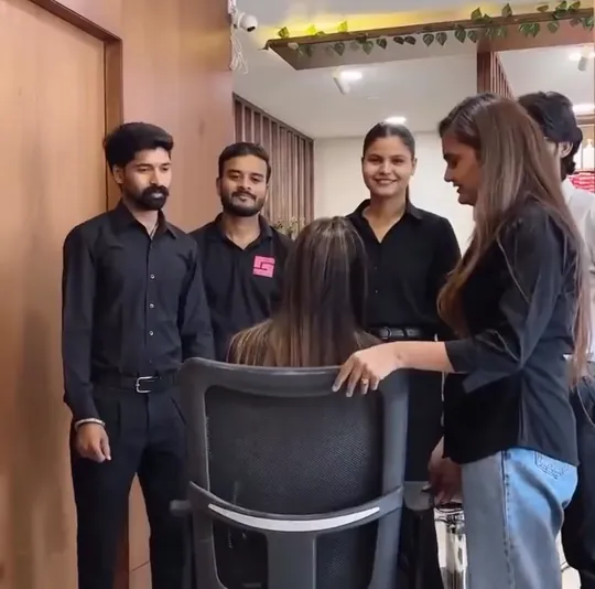 Six staff members posed in a wood-panelled corridor of the salon, all in dark clothing: a woman in a black blazer at the left, two men in black shirts, a woman .