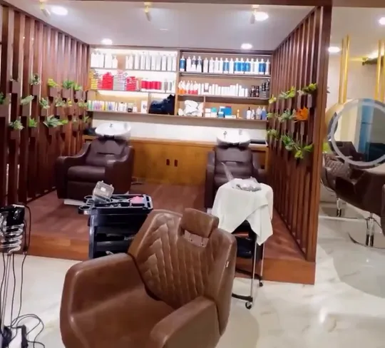 A slow pan across the empty salon floor showing two wash-station recliners, a wooden slat partition hung with small planters, lit shelves of product and a round backlit mirror.